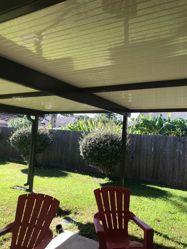 Covered patio with two red chairs overlooking a sunny backyard and wooden fence