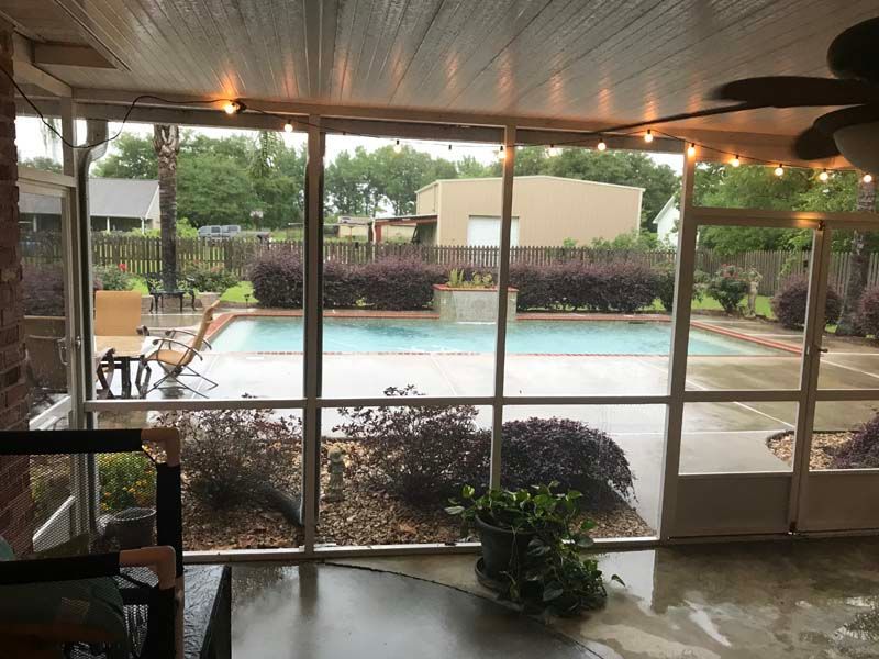 Screened patio overlooking a backyard pool and garden, with patio furniture and potted plants