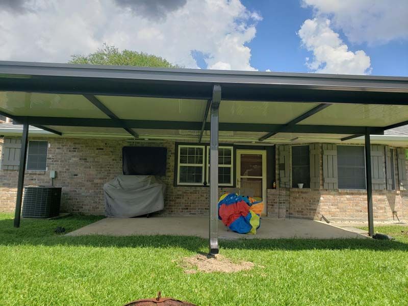 Covered front porch with brick walls, a black pillar, lawn in front, and colorful items near the door.