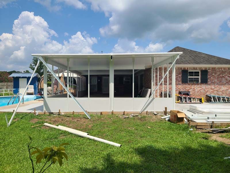 White patio extension under construction beside a brick house, with scaffolding and materials in a backyard.