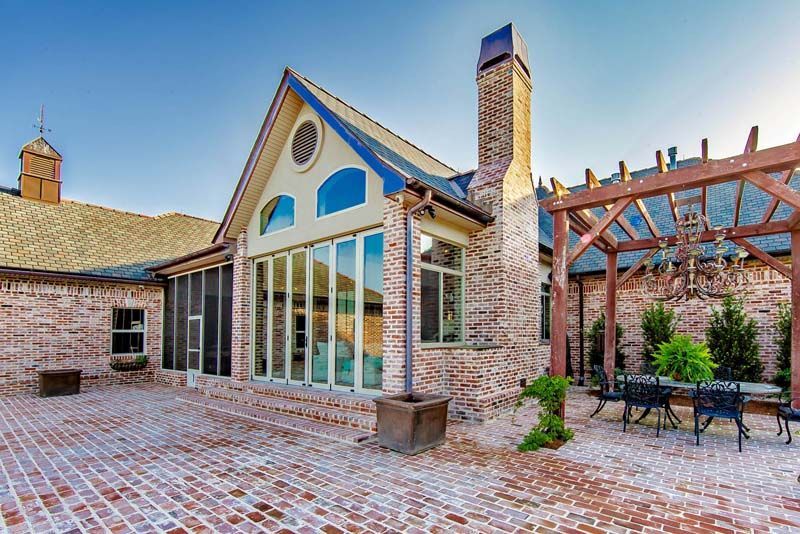 Brick courtyard patio with a stone house, large windows, pergola, and outdoor seating