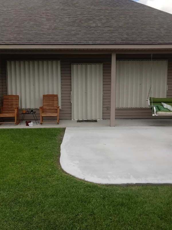 Patio with sliding doors, two wooden chairs, and a white concrete slab beside a green lawn.