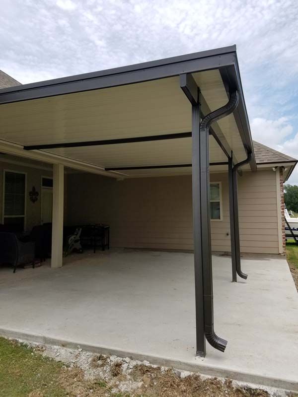 Covered concrete patio with beige roof and dark support posts beside a house