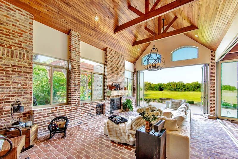 Spacious brick-and-wood living room with large windows, high vaulted ceiling, and white seating overlooking green fields