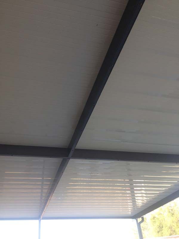 Close-up of a gray metal roof with dark support beams and bright sunlight filtering through the edge