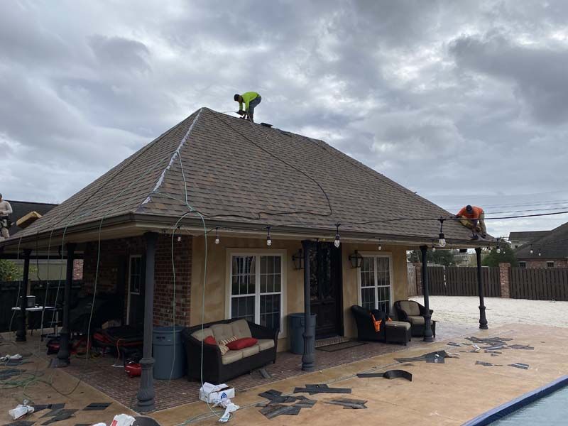 Two workers on a rooftop above a patio, one in green and one in orange, under a cloudy sky.