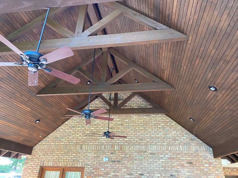 Wooden cathedral ceiling with exposed beams and three ceiling fans above a brick wall