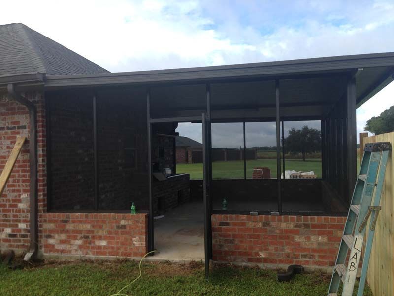 Brick house porch with large windows and open doorway, viewed from the front yard.