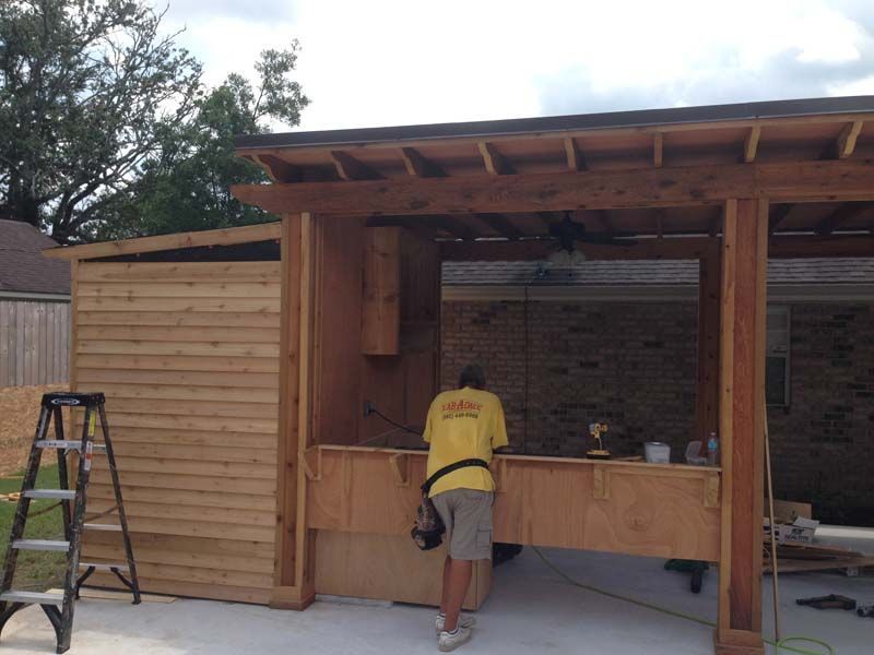 Person working at an outdoor wooden bar or kitchen under construction with a ladder nearby