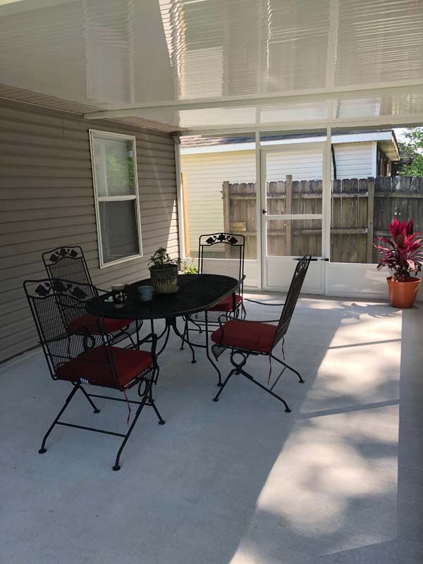 Covered patio with black metal table and chairs, potted plants, and sliding glass doors