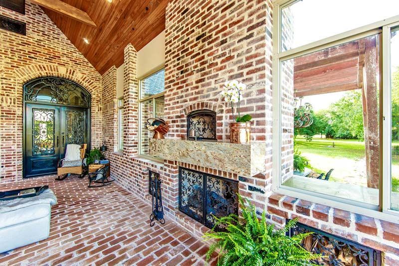 Brick-and-wood porch with fireplace, seating, and open view of a green yard