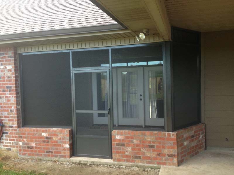 Brick storefront entrance with screened door and windows under a covered porch