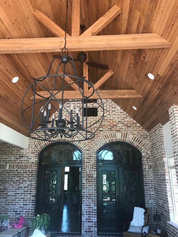 Brick entryway with arched double doors, wooden ceiling beams, and a black wrought-iron chandelier dangling overhead