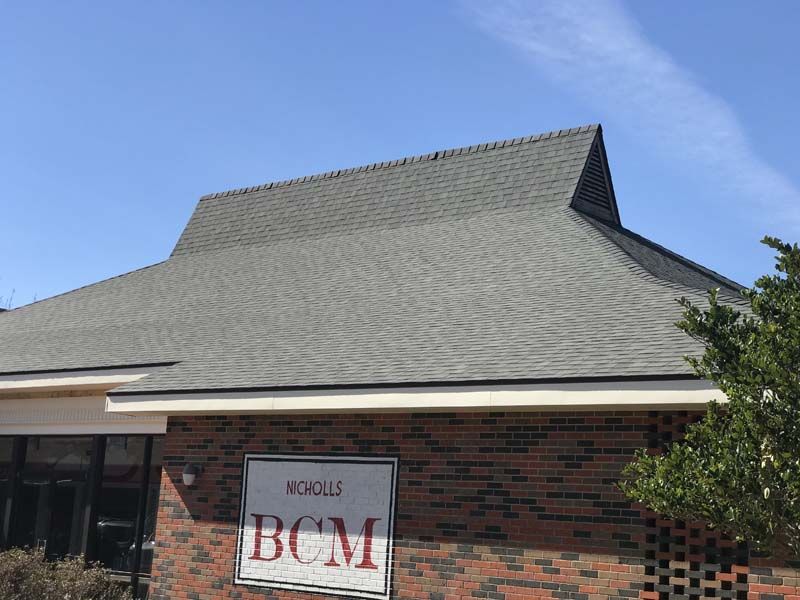 Brick building with a gray roof and a “BCM” sign beneath a blue sky