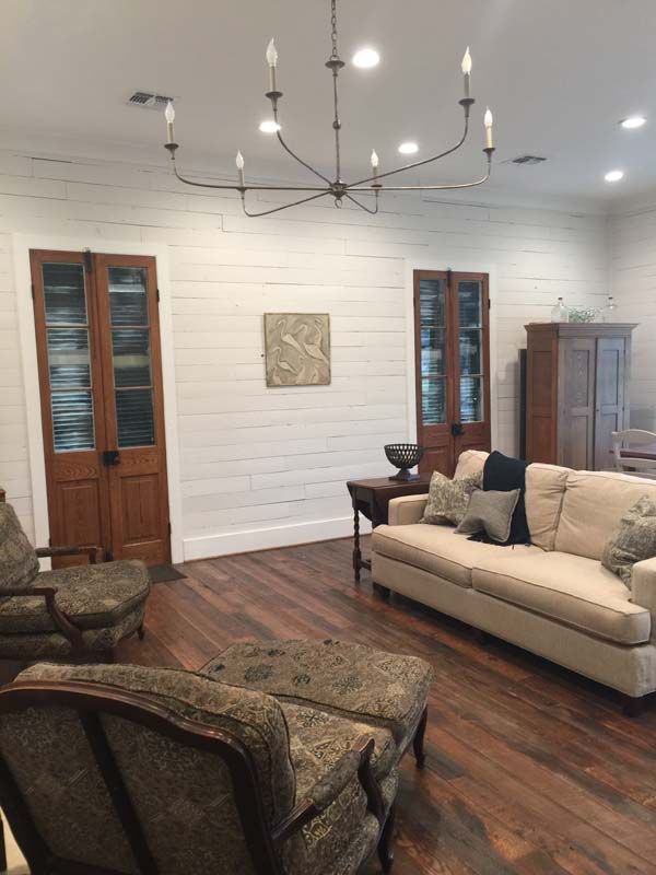 Cozy living room with beige sofa, patterned chairs, chandelier, wood doors, and white shiplap walls