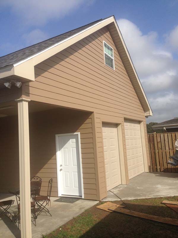 Tan house exterior with white garage doors, front porch, and a white side door under a blue sky.