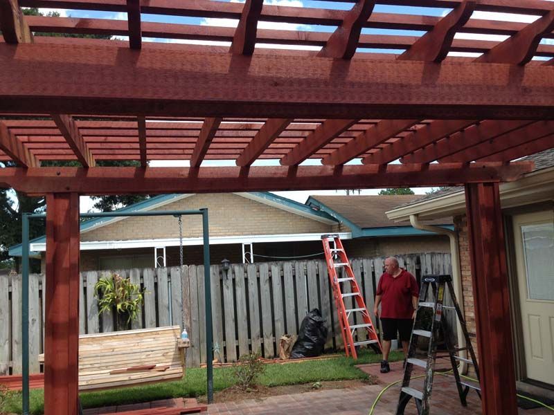 Two workers on ladders under a red pergola, building a backyard patio or deck structure.