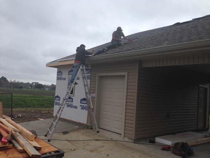 Two workers on a roof using ladders beside a house under construction