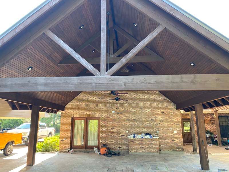 Covered brick entryway with wood-beam roof and double glass doors, flanked by columns and a parked truck.