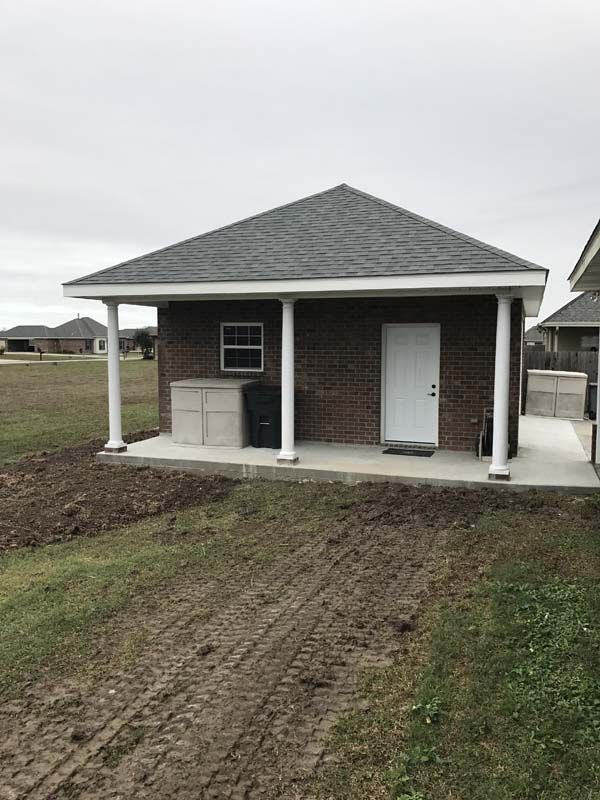 Small brick outbuilding with white door and porch, set on a grassy lot under an overcast sky.