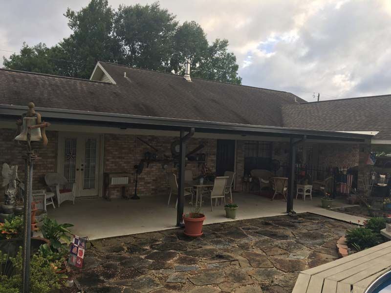 Covered stone patio with porch furniture, potted plants, and a hanging birdcage under a house roofline.