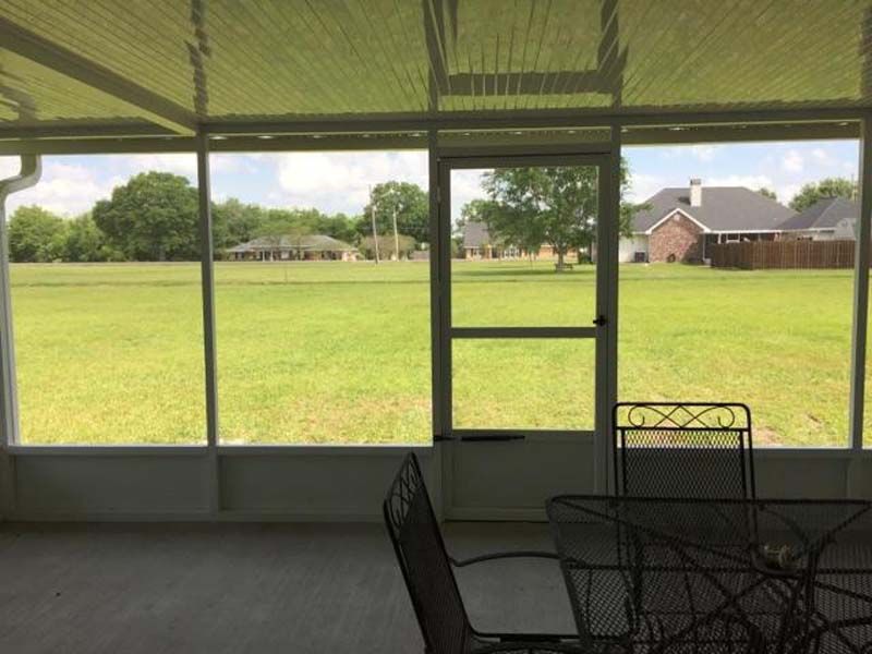 Screened porch overlooking a green field and houses, with patio chairs in the foreground.