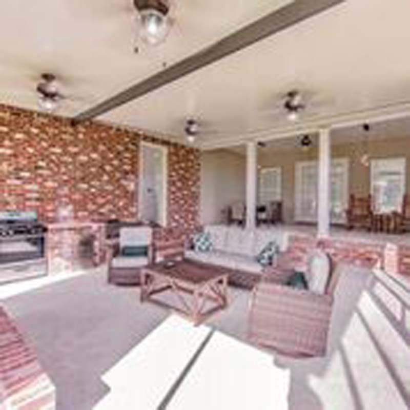 Bright patio lounge with wicker seating, brick accent wall, and large windows under a covered roof