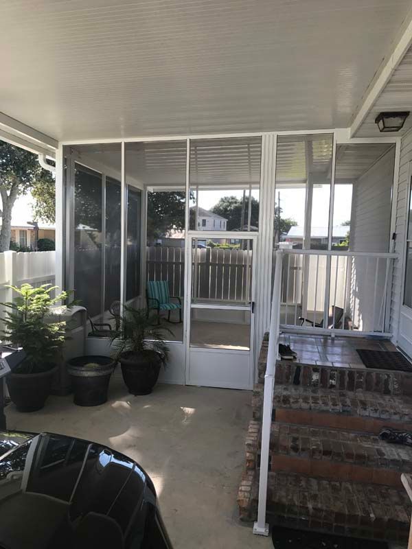 Covered porch with white railing, potted plants, and a brick grill beside sliding glass doors