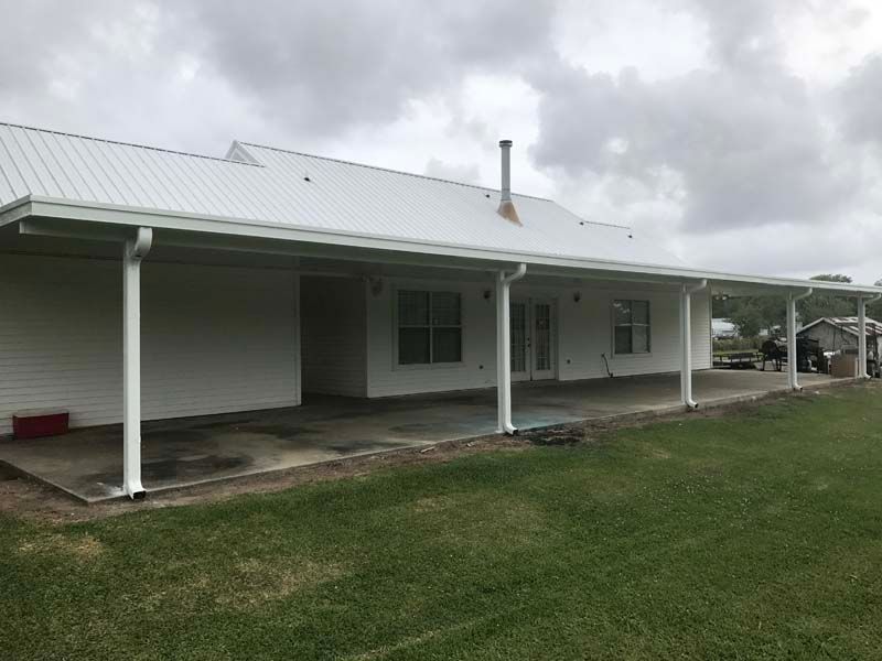 Single-story white house with a metal roof and covered porch on a grassy lawn under cloudy skies