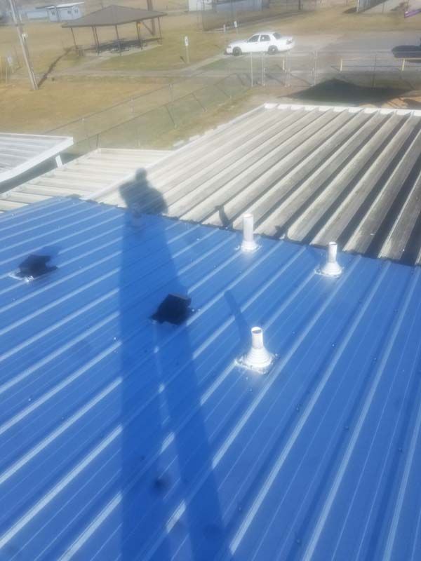 Blue and gray metal roof with vents, seen from above with a shadow and parking lot in the background