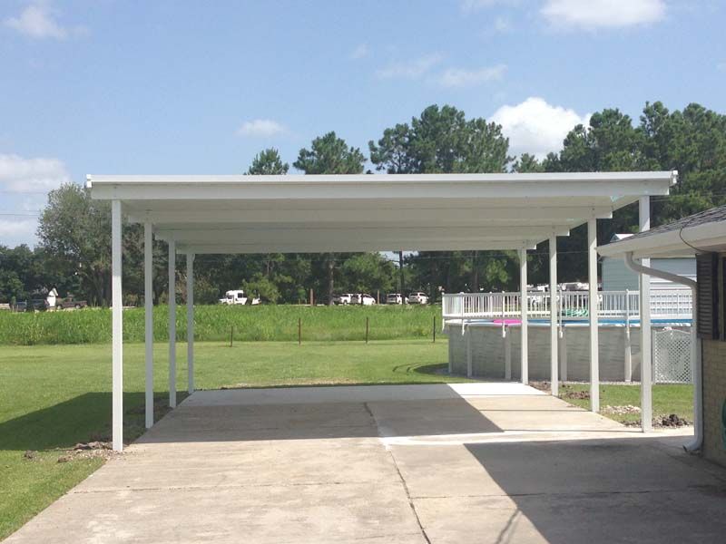 Covered parking area with white metal roof beside a paved walkway and grassy field