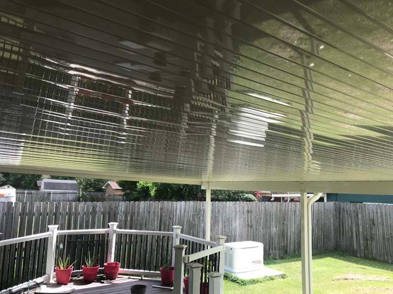 Back patio with a white pergola roof, fence, potted plants, and a hot tub on a grassy yard.