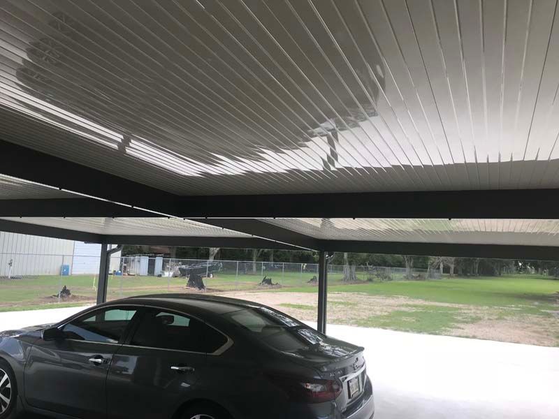 Dark car parked under a metal carport beside a grassy lot