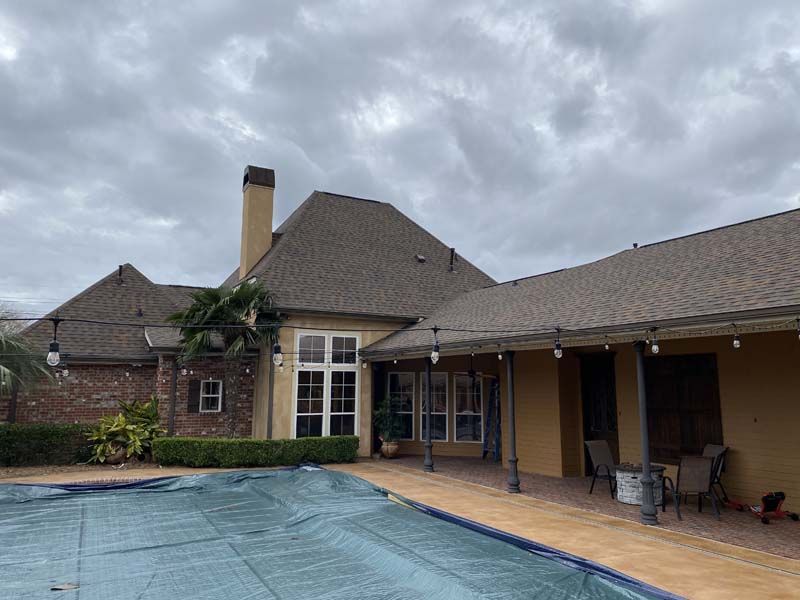 Backyard patio and covered seating area beside a house, with a pool covered by a blue tarp under cloudy skies