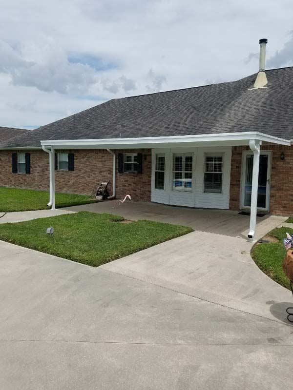 Brick house front porch with white columns, gray roof, driveway, and small lawn under cloudy sky