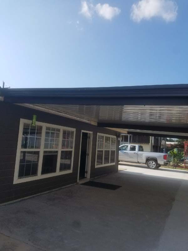 Driveway under carport beside dark house, with a white pickup truck parked in back.