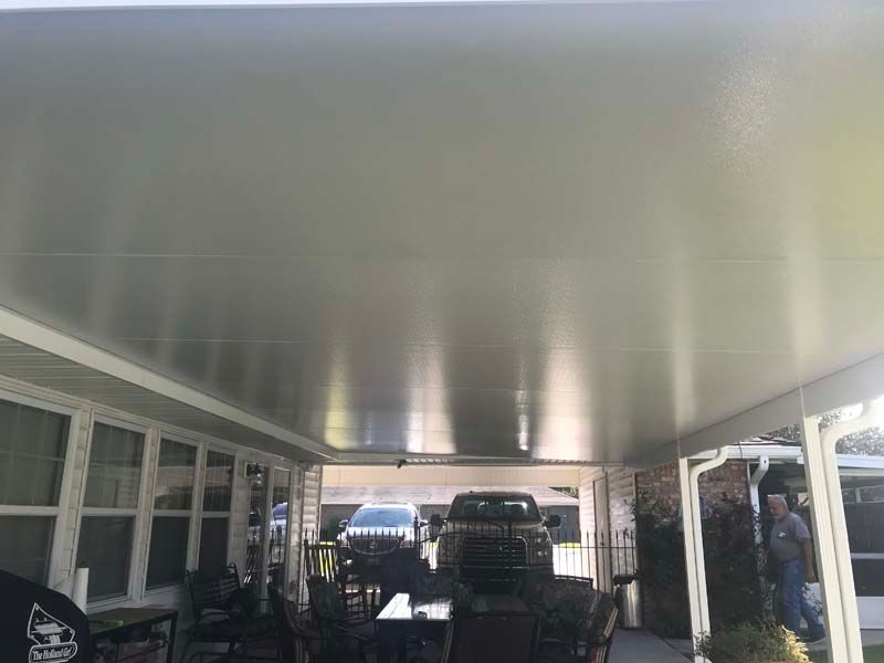 Covered carport with parked vehicles and people standing along the side.
