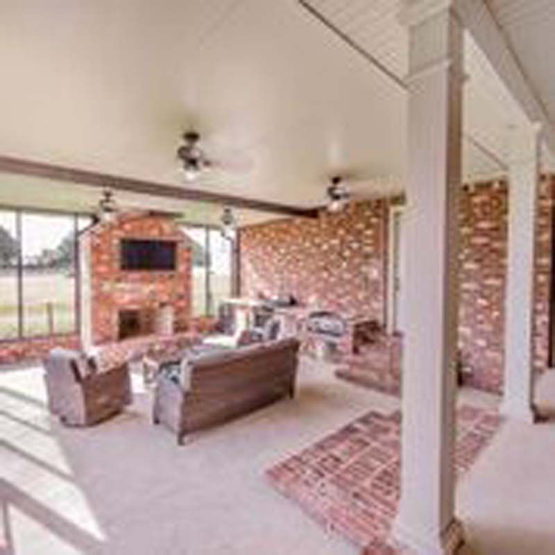 Covered patio with brick fireplace, ceiling fans, and seating area overlooking a yard.