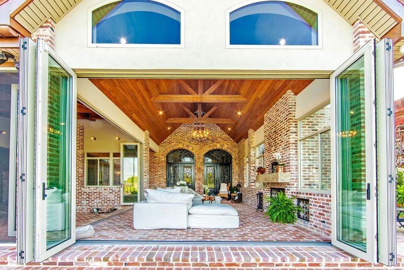 Open French doors to a bright brick patio with white seating and a vaulted wooden ceiling