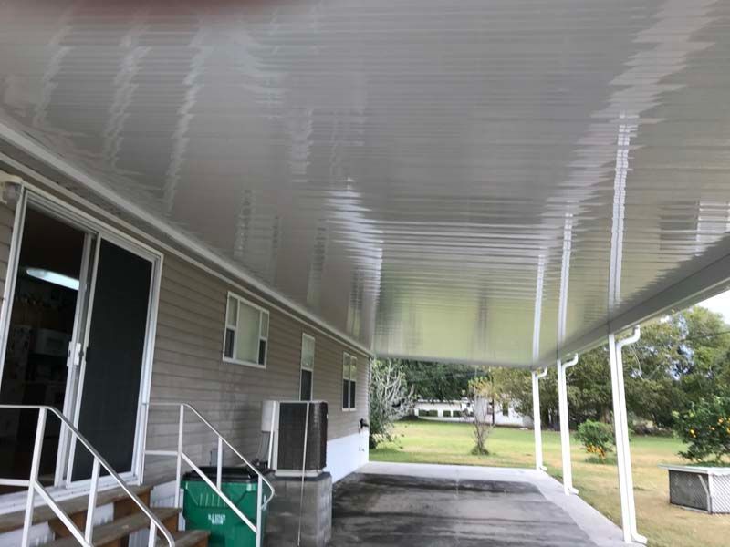 Covered apartment walkway with white columns, doors, windows, and green lawn beyond