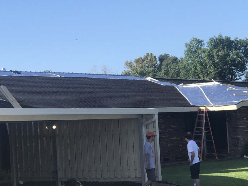 Solar panels being installed on a house roof, with two workers and a ladder visible below.