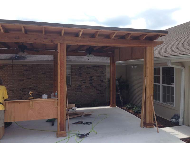 Partially built wooden patio cover beside a house, with exposed beams and construction materials on the floor