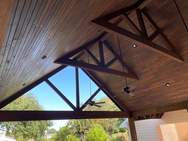 Wooden pavilion ceiling with exposed beams, ceiling fans, and skylights over an open patio
