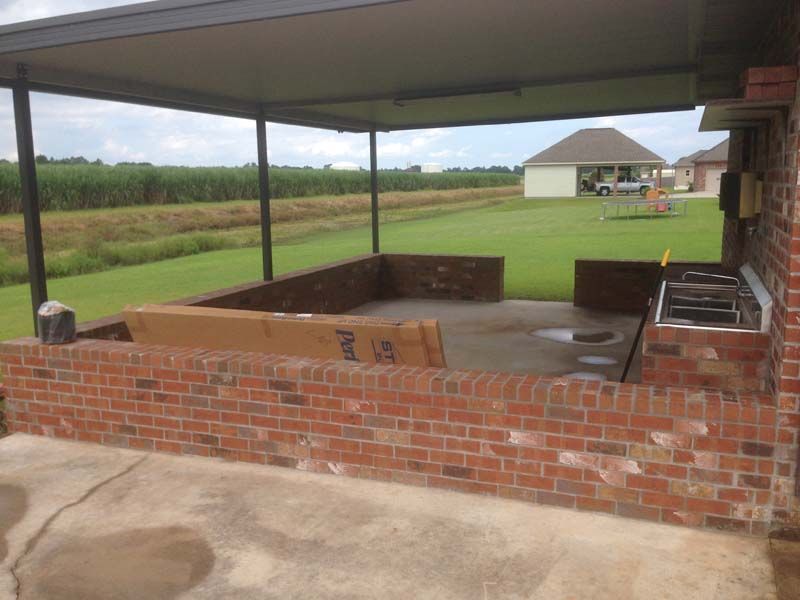 Covered brick outdoor patio with a low wall, concrete floor, and grassy yard beyond.