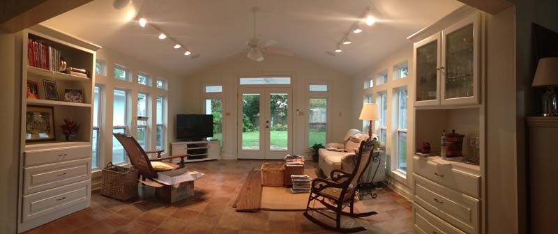 Bright living room with large windows, beige decor, sofa, rocking chair, TV, and bookshelves