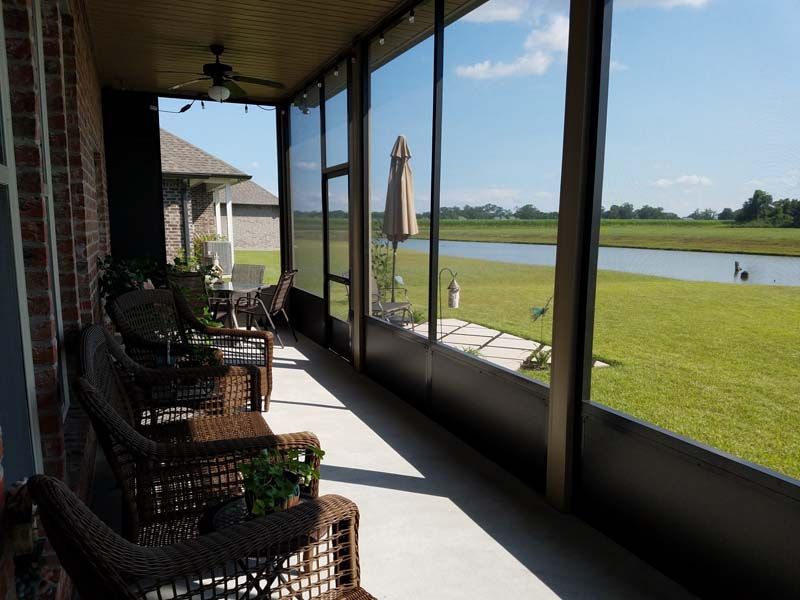 Screened porch with wicker chairs overlooking a grassy yard and water under a blue sky