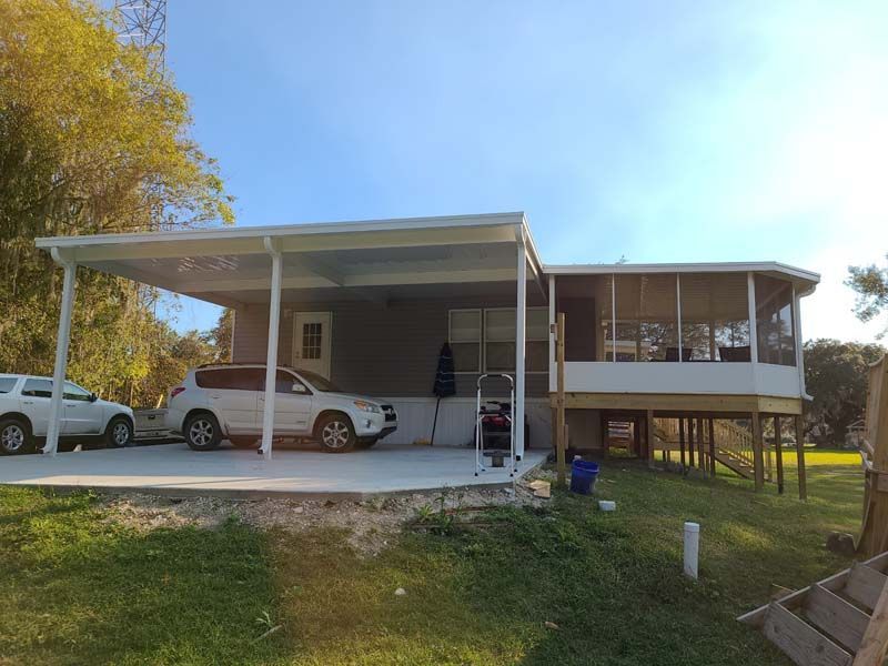 House on stilts with a covered carport, two parked cars, and a person near the front steps.