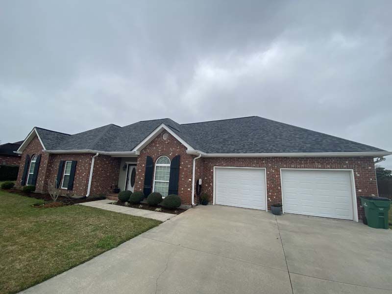 Brick suburban house with two white garage doors and a wide concrete driveway under cloudy skies