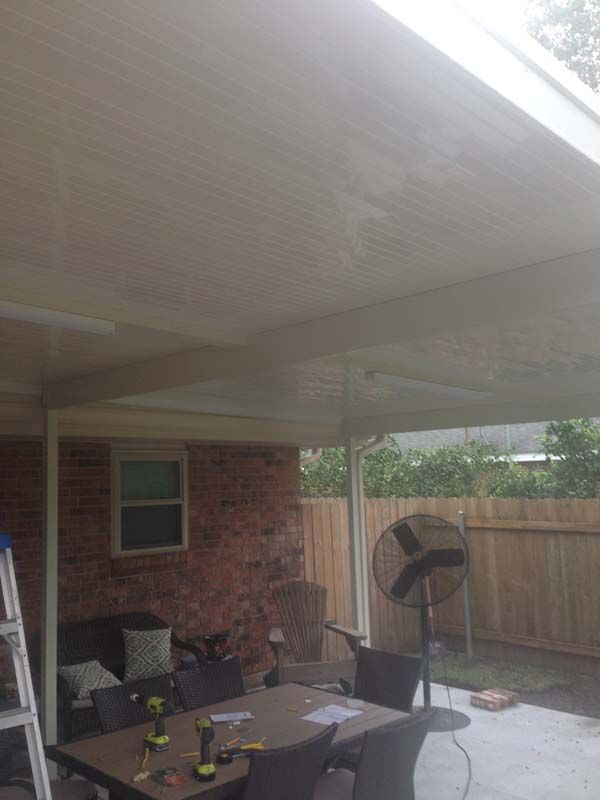 Covered patio with outdoor seating, fan, brick wall, and fenced yard in the background
