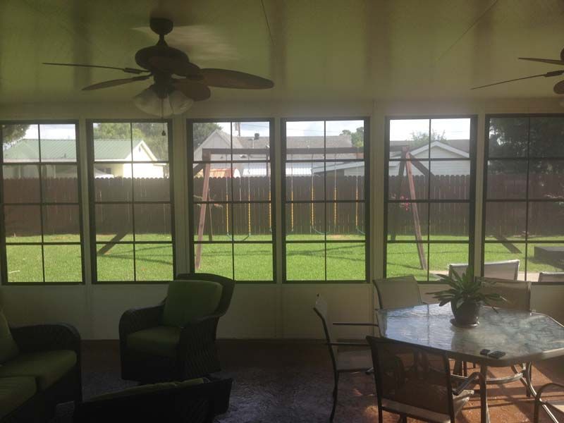 Sunroom with large windows, ceiling fans, and patio furniture overlooking a green backyard and fence.